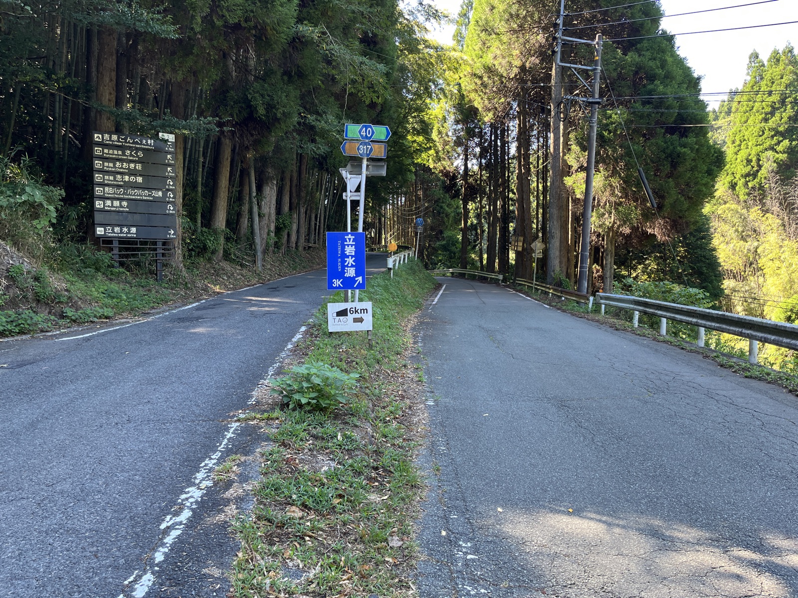 県道40号の分岐に立つ案内標識。青い「立岩水源」の看板の下に、TAOの「6km →」と書かれた白い小さな看板が出ている