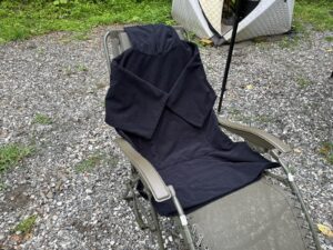 ミキタオサウナで貸し出しているフード付きのタオル地サウナポンチョを、砂利の上の外気浴チェアに掛けたところ。奥はテントサウナ