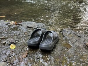 荻の草川の際の濡れた岩の上に、ミキタオサウナのレンタルサンダルを脱いで並べて置いたところ。奥に川が流れている