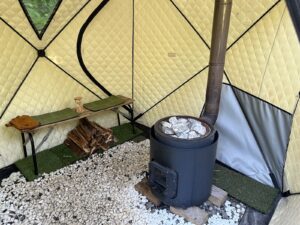 ミキタオサウナのテントサウナ内部。木のベンチに10分計の砂時計を置き、右側にサウナストーンを載せた薪ストーブがある