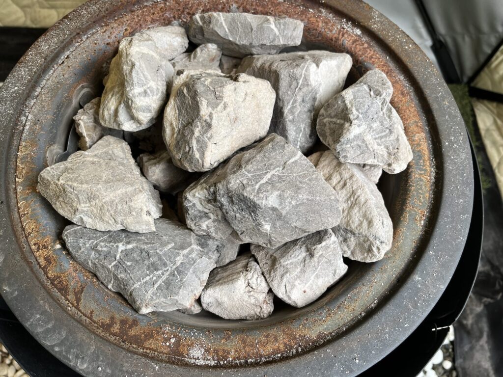 テントサウナの薪ストーブの天板を上から見たところ。丸いバスケットに、白っぽく粉をふいた交換前のサウナストーンが積まれている。