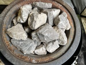 テントサウナの薪ストーブの天板を上から見たところ。丸いバスケットに、白っぽく粉をふいた交換前のサウナストーンが積まれている。
